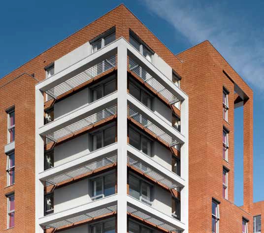 Fully glazed communal areas are positioned on the corner, with balconies expressed in white render in contrast to the brickwork